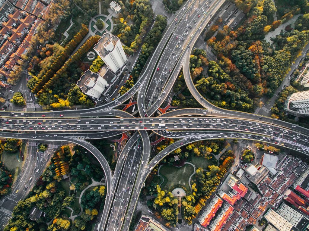 Luftaufnahme eines komplexen, mehrstöckigen Autobahnkreuzes in einer chinesischen Metropole mit dichtem Verkehrsaufkommen; die erhöhte Perspektive ermöglicht trotz des scheinbaren Chaos eine klare Übersicht über die Verkehrsströme und Verbindungen.